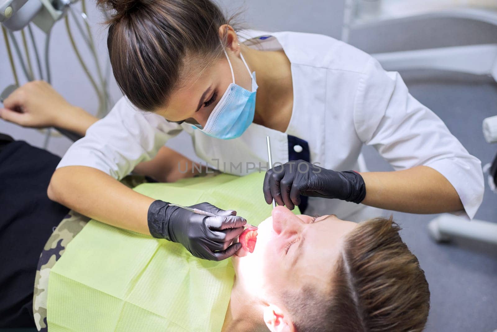Female dentist treating teeth to patient, young man in chair at dental clinic.