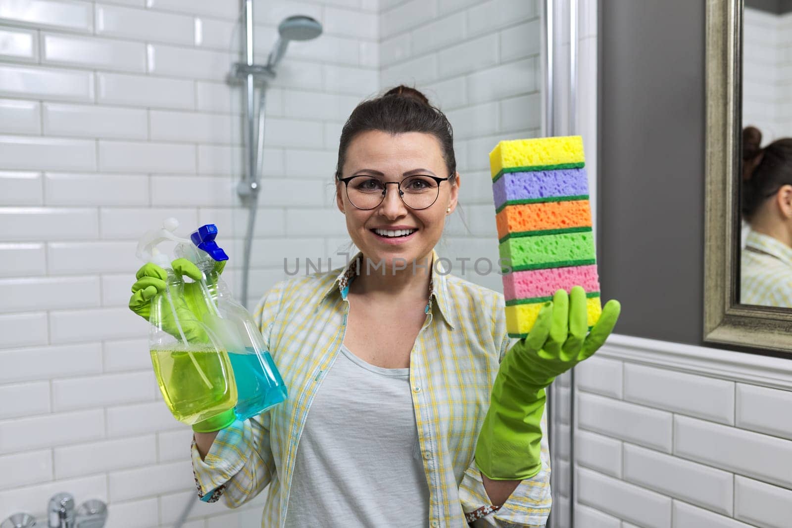 Woman cleaning at home in bathroom holding detergents and sponges by VH-studio