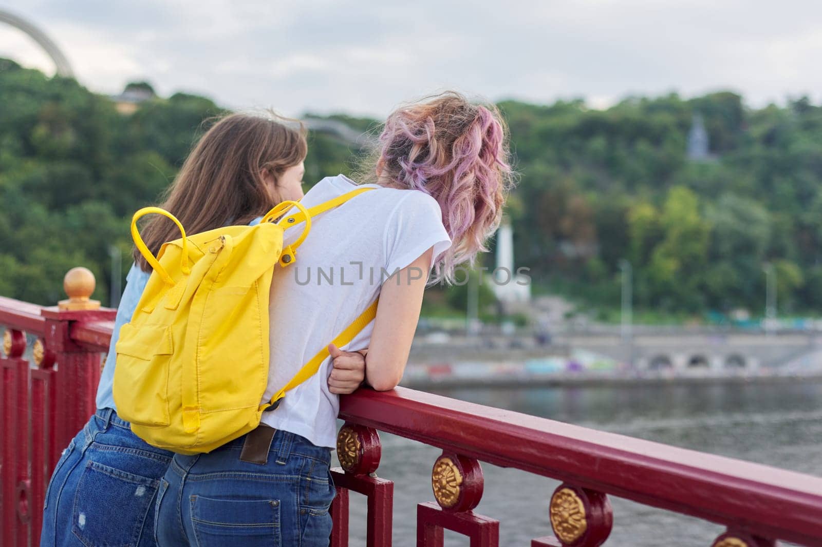 Portrait of two teenage girls standing with their backs on bridge over river by VH-studio