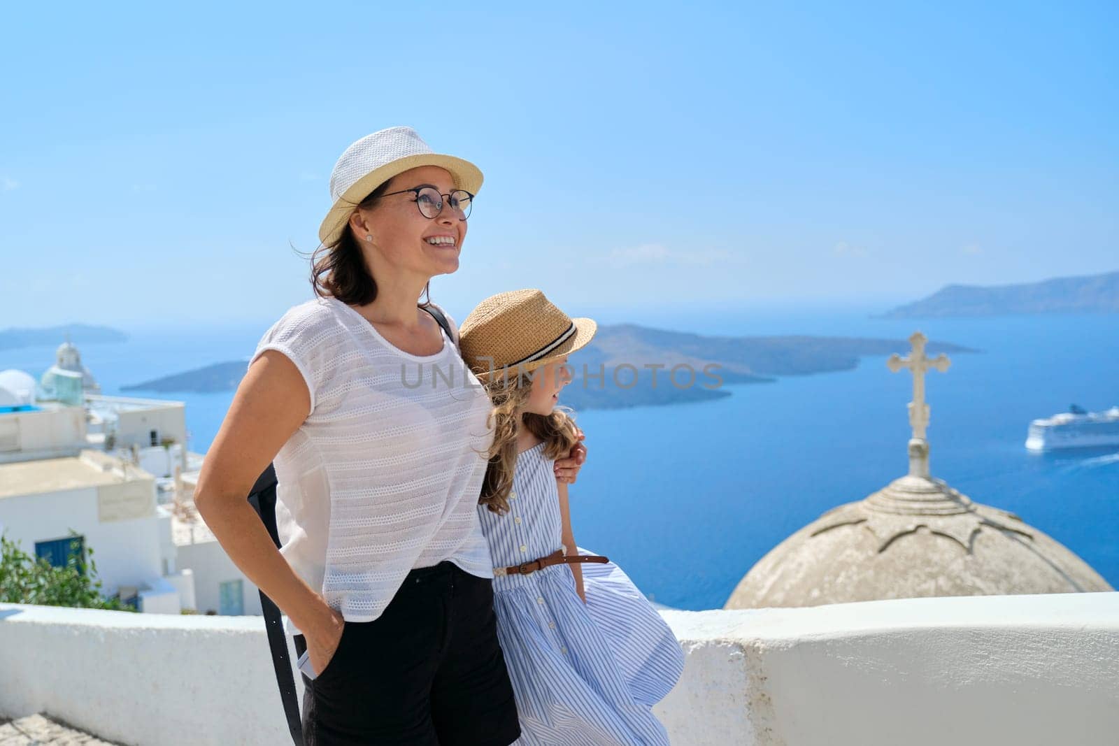 Mother and daughter child, happy traveling family walking together, holding hand on the famous tourist Greek island of Santorini. Sky, sea, church dome background