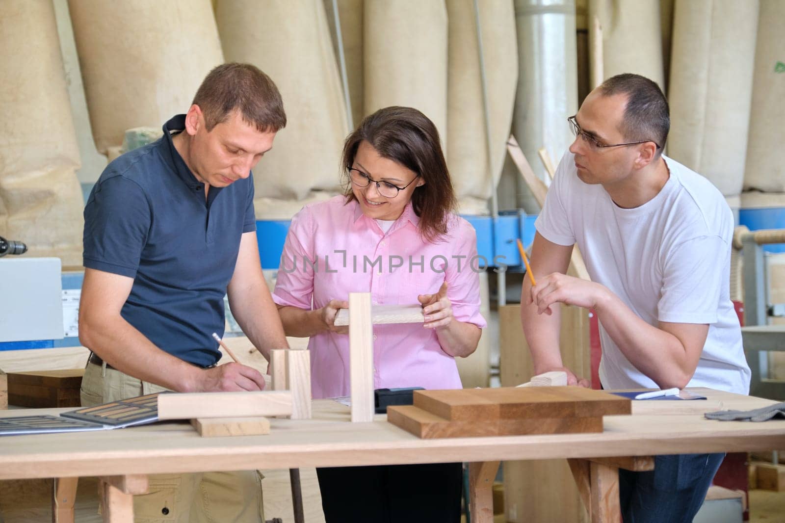 Group of industrial people client, designer or engineer and workers working together on project of wooden furniture. Teamwork in carpentry workshop