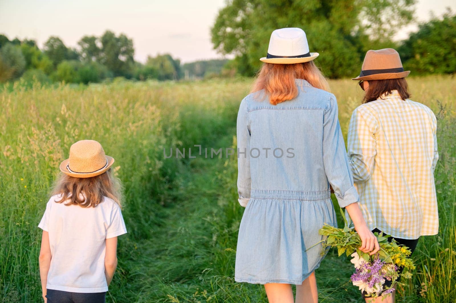 Mother and children two daughters walking along a country road through a meadow. Summer, nature, family, vacation