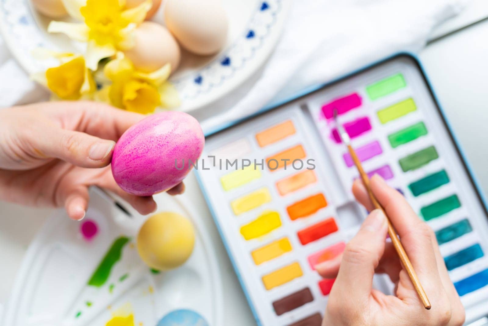 A brush in the process of painting Easter eggs with watercolors. The concept of preparing for Easter. View from above. by sfinks