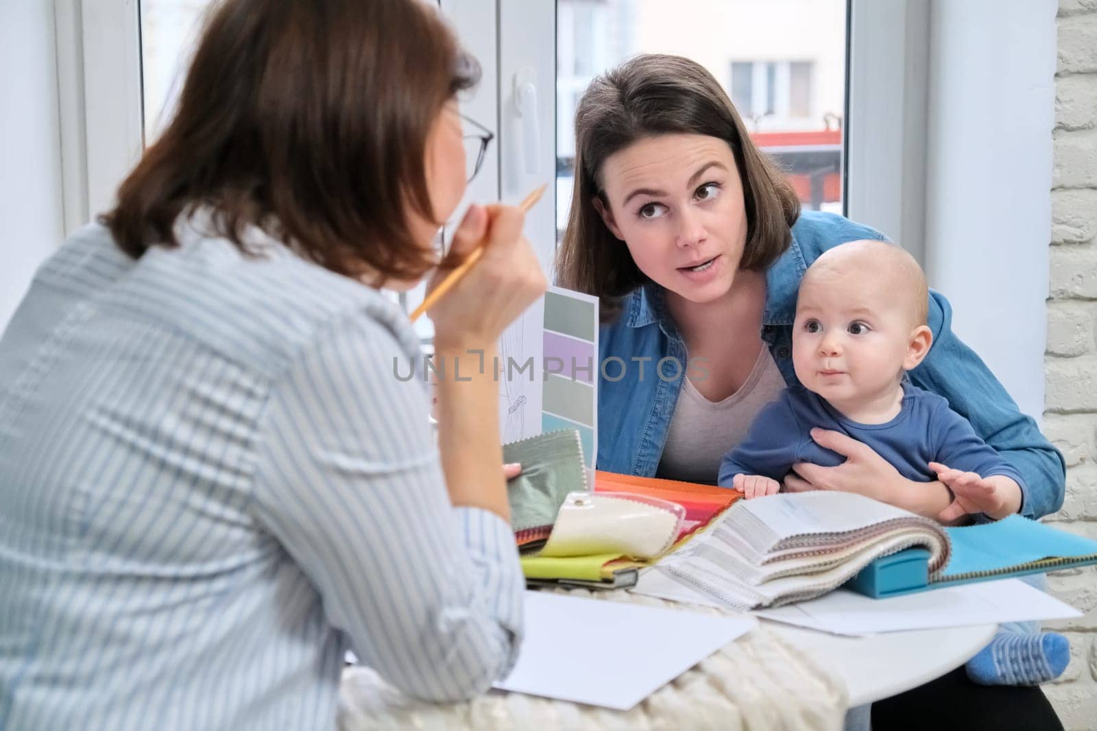 Women interior designer and client with baby choosing fabrics and materials.