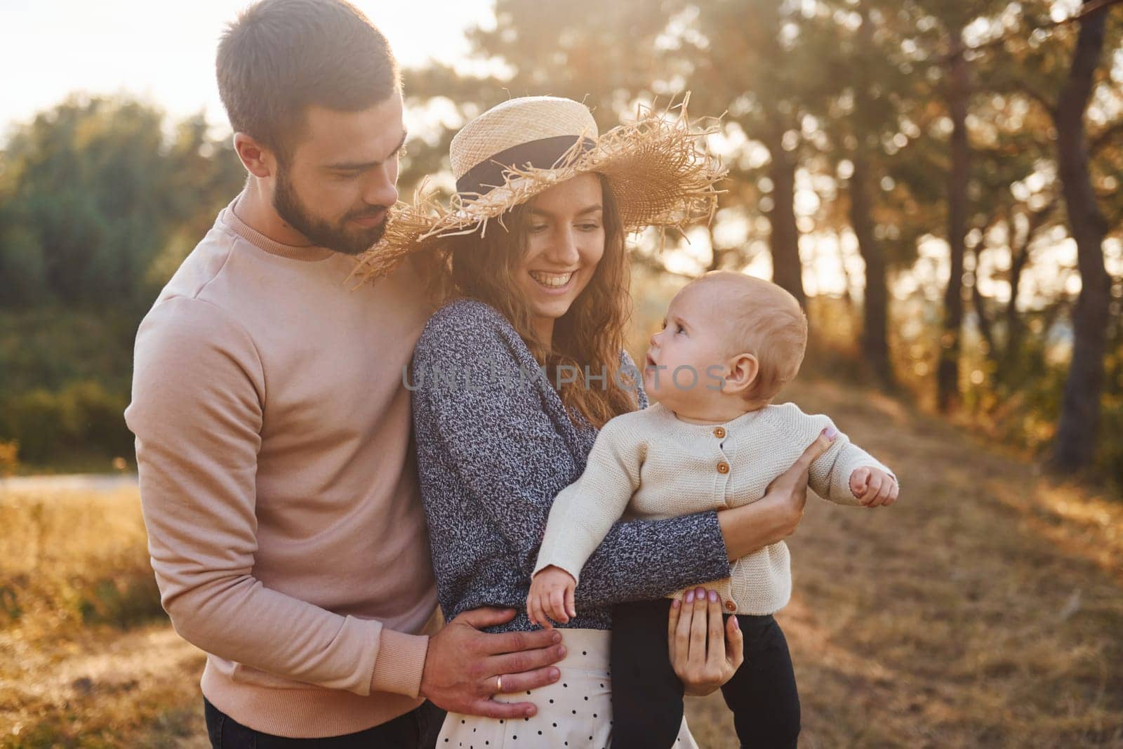 Happy family of mother, family and little baby rests outdoors. Beautiful sunny autumn nature.