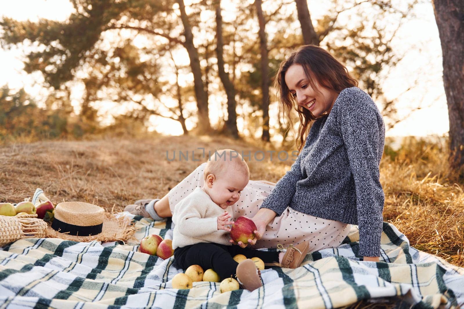 Young mother with her little baby rests outdoors at autumn season.