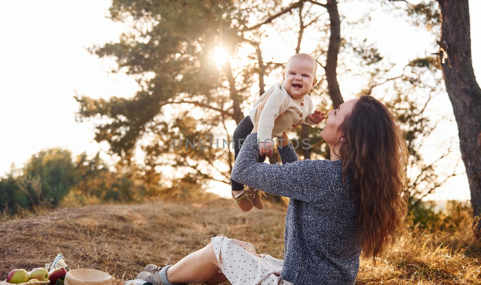 Young mother with her little baby rests outdoors at autumn season.