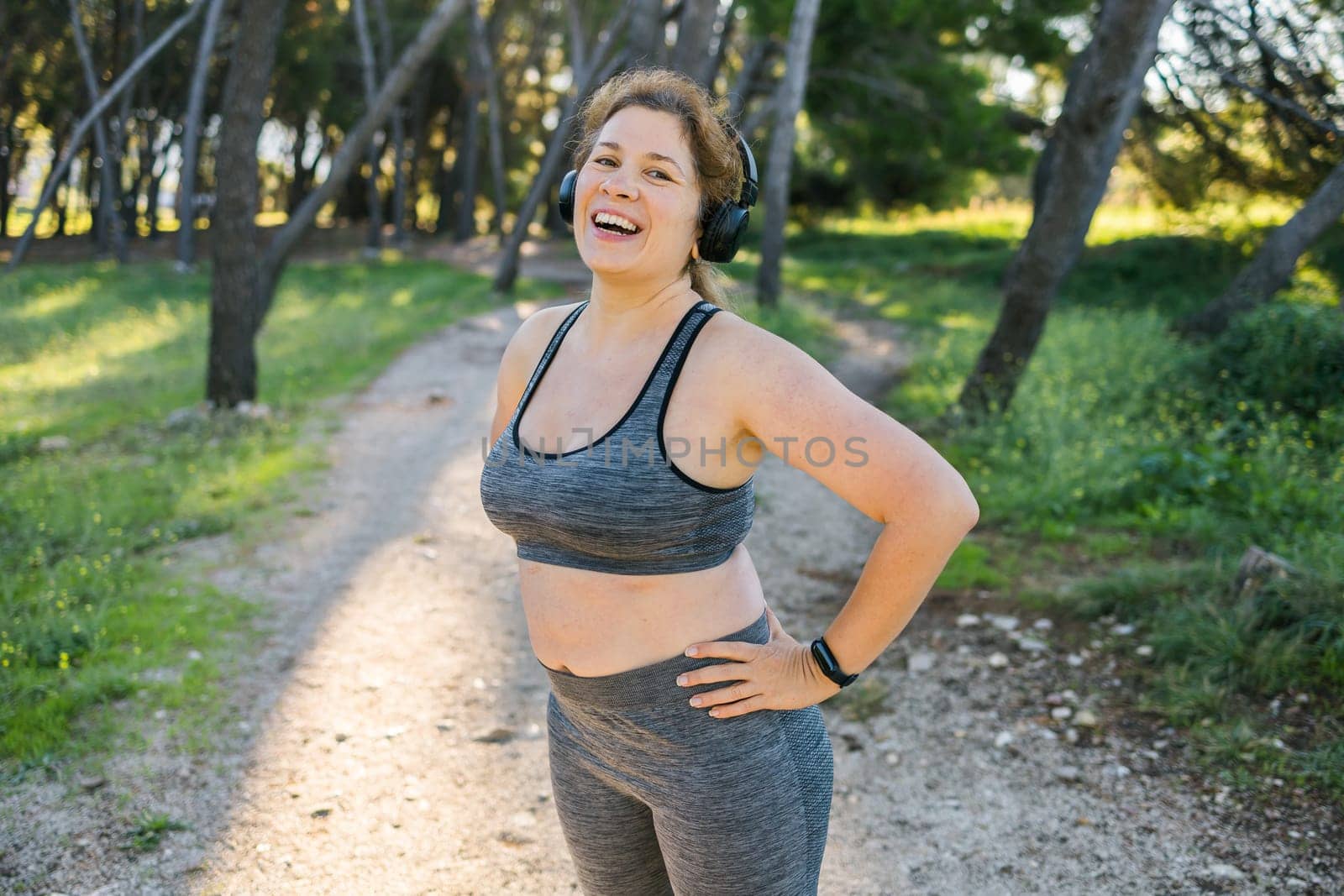 Fat woman and sports. Girl doing exercise for weight loss in the fresh air and laughing in camera after training. Copy space and empty space for text or advertising by Satura86