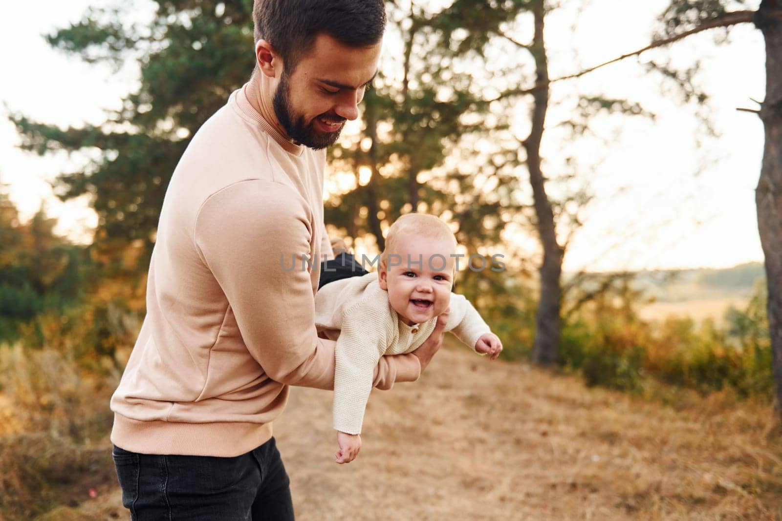 Bearded father playing with his child outdoors at sunny daytime outdoors.
