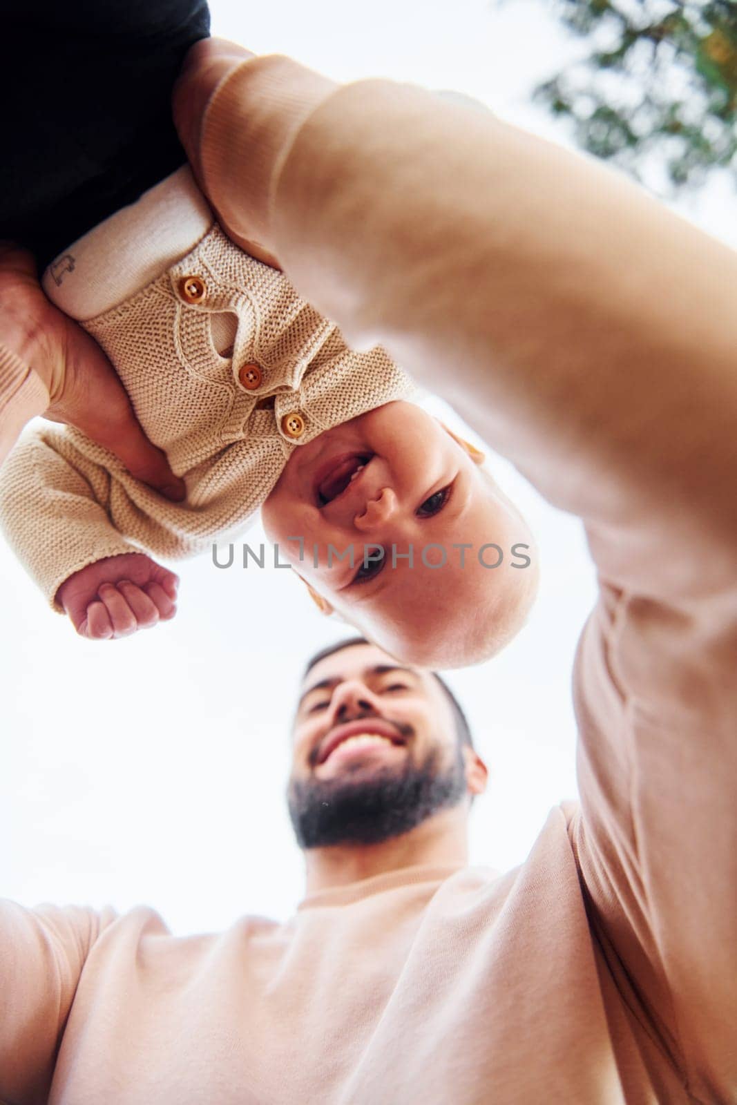 Bearded father playing with his child outdoors at sunny daytime outdoors.
