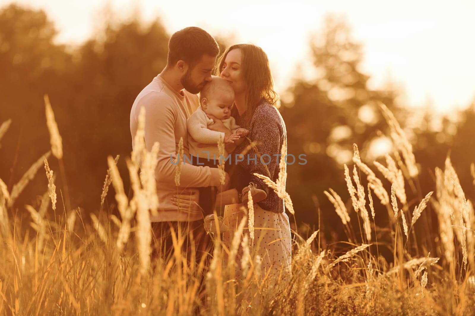 Illuminated by sunlight. Happy family of mother, family and little baby rests outdoors. Beautiful sunny autumn nature.