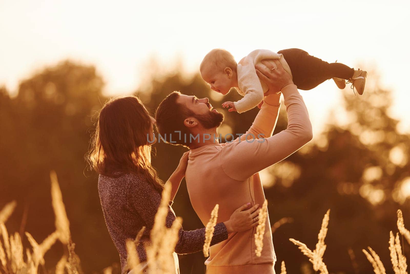 Illuminated by sunlight. Happy family of mother, family and little baby rests outdoors. Beautiful sunny autumn nature.