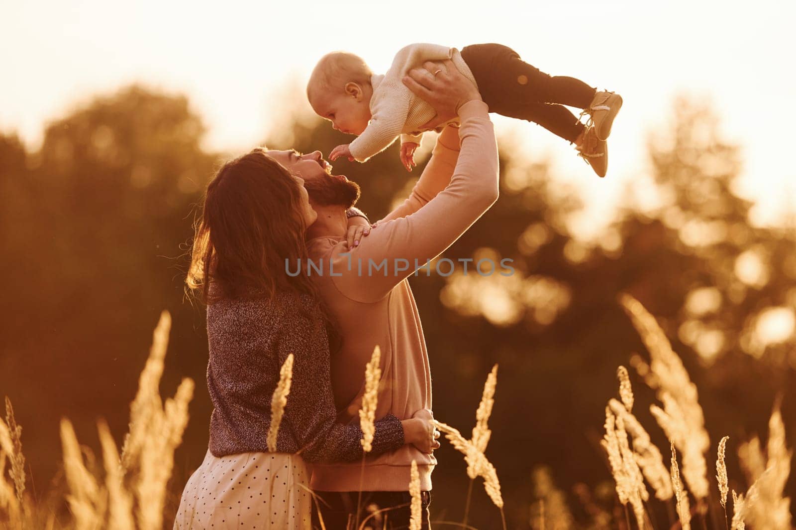 Illuminated by sunlight. Happy family of mother, family and little baby rests outdoors. Beautiful sunny autumn nature.