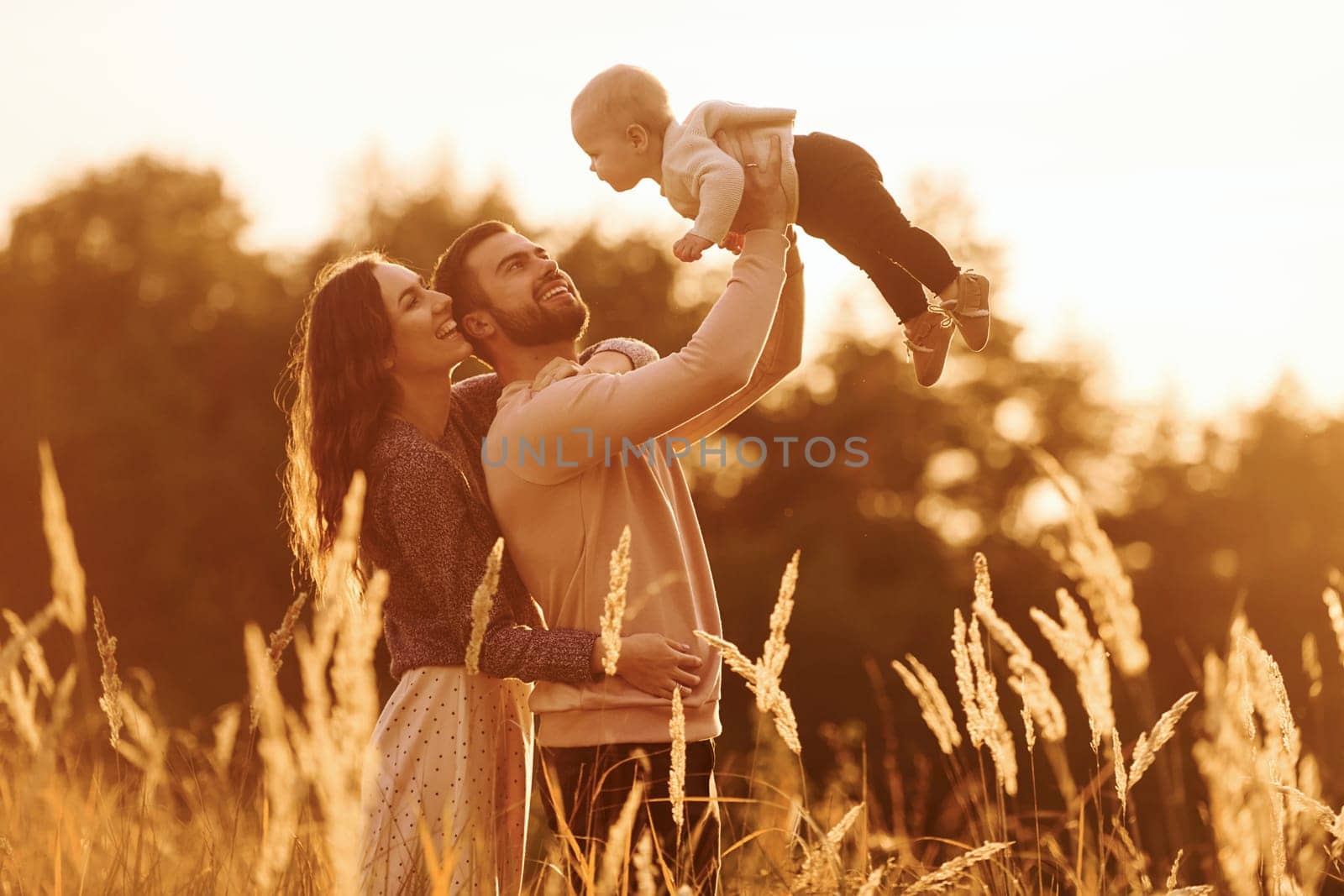 Illuminated by sunlight. Happy family of mother, family and little baby rests outdoors. Beautiful sunny autumn nature.