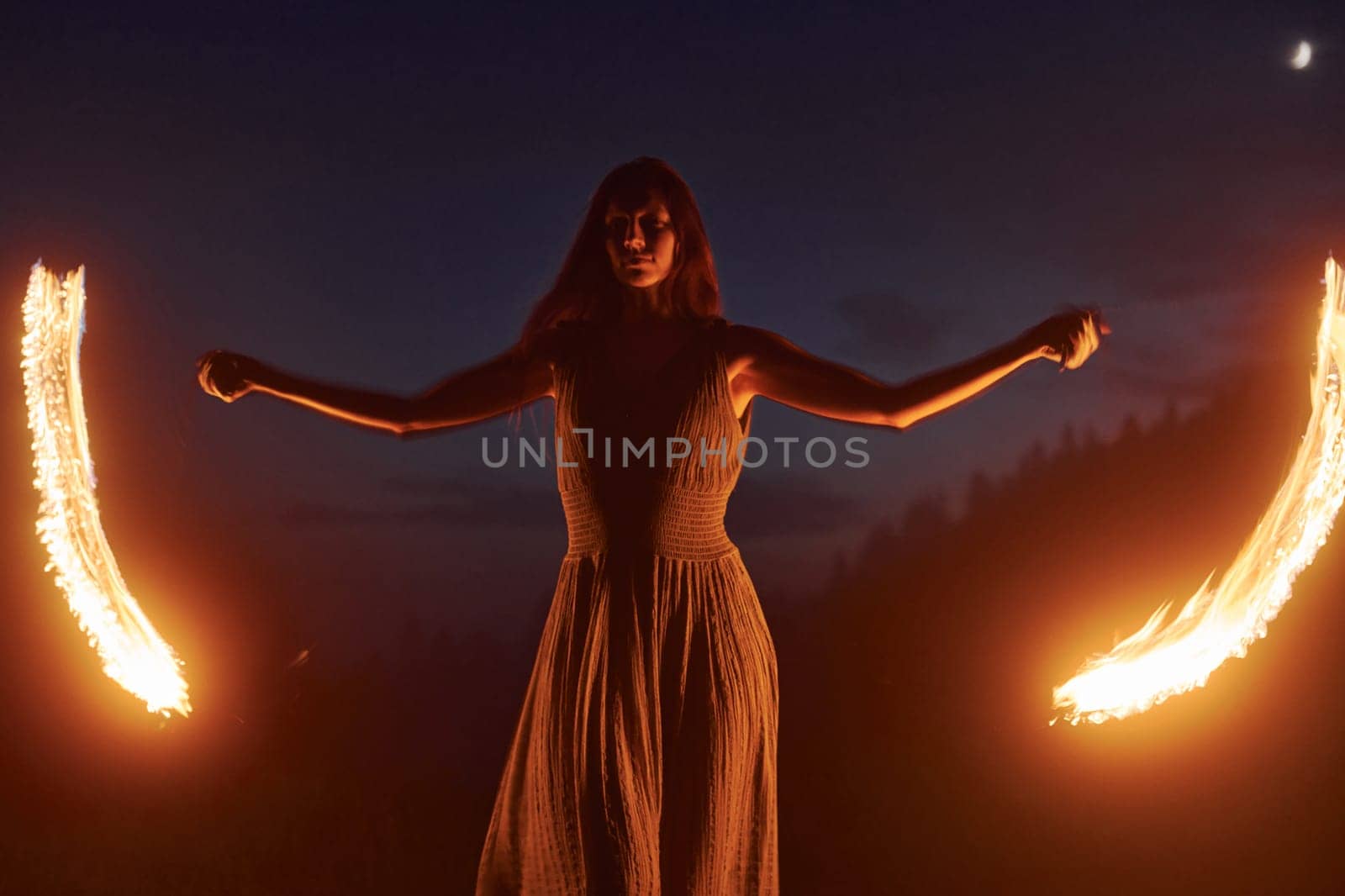 Photo with a long exposure. Fire show by woman in dress in night Carphatian mountains. Beautiful landscape.