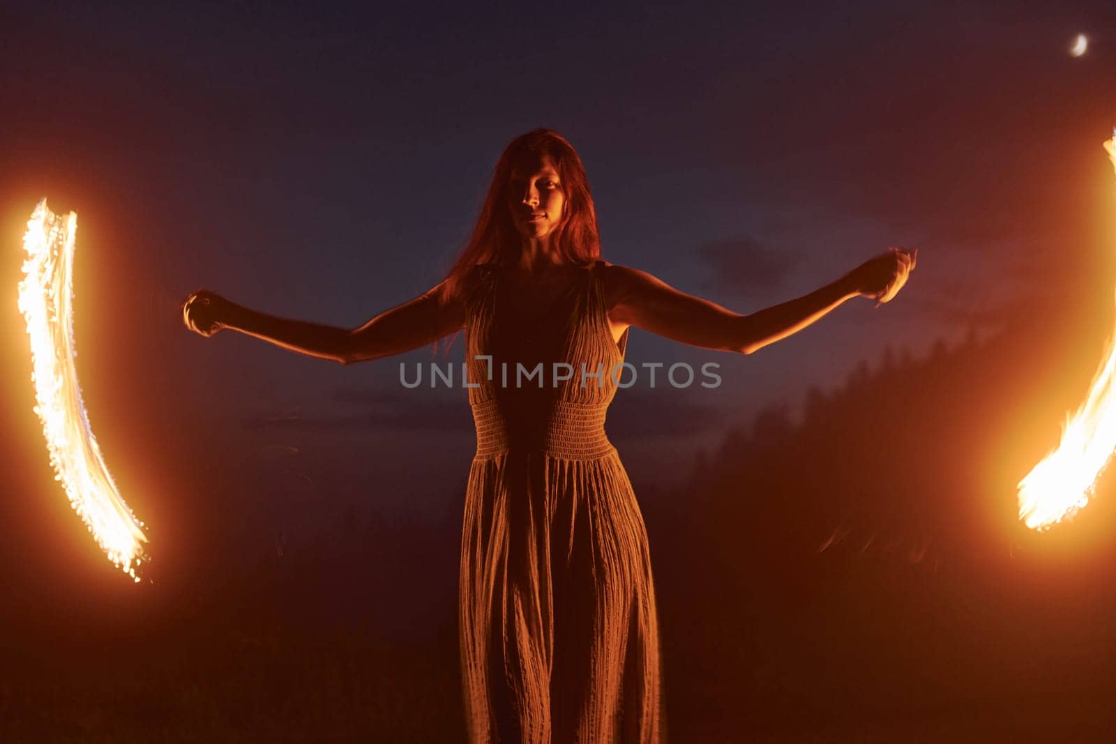 Photo with a long exposure. Fire show by woman in dress in night Carphatian mountains. Beautiful landscape.