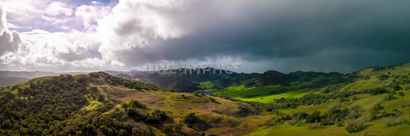 Panoramic view of bright sun and dark storm clouds over green California landscape by Osaze