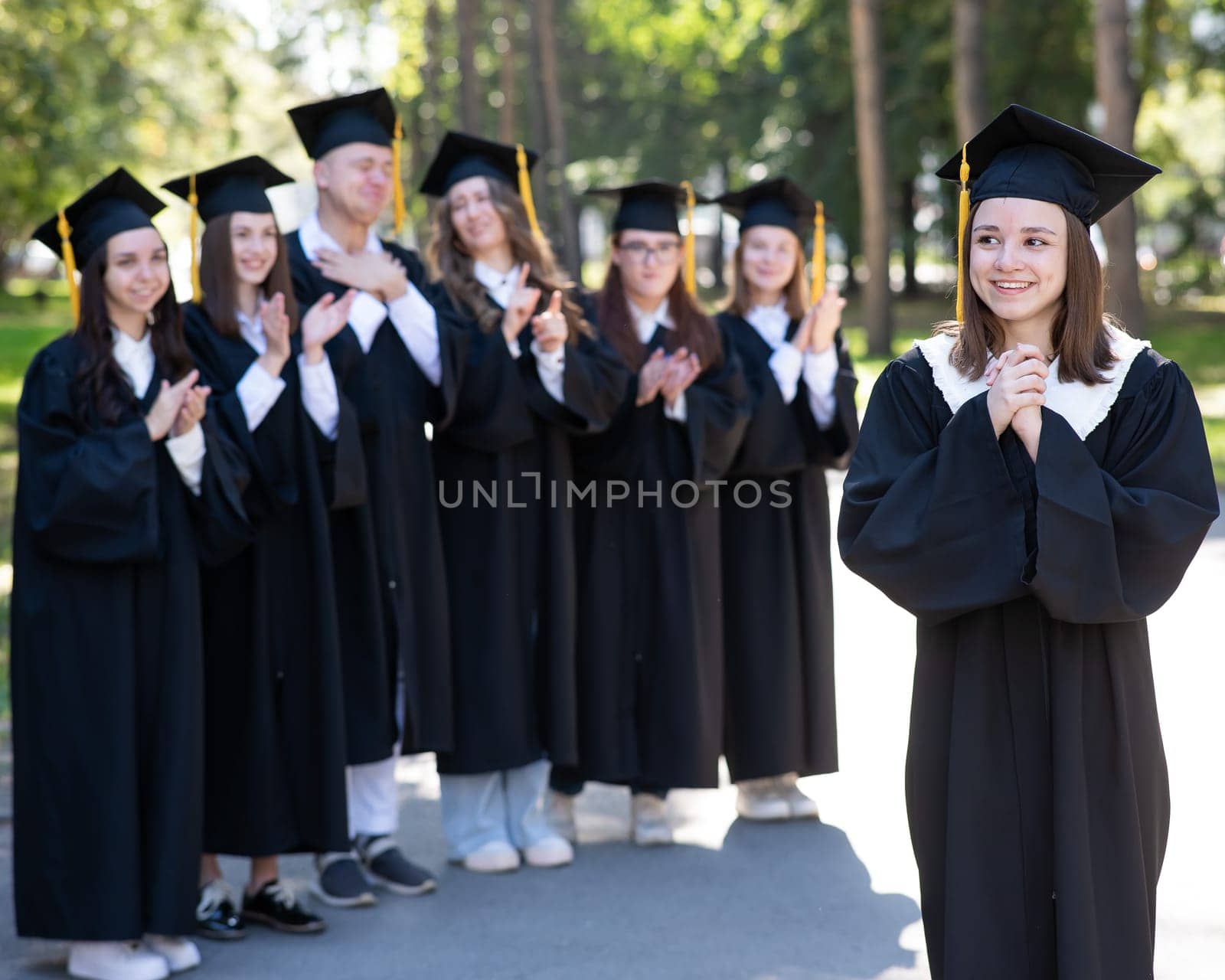 Group of happy students in graduation gowns outdoors. A young girl in the foreground