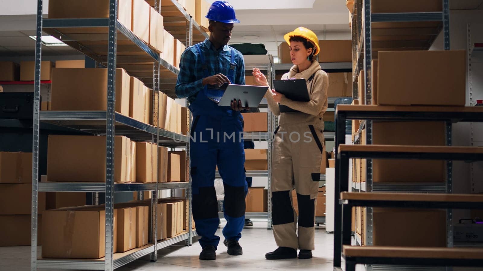 Two depot workers doing inventory for warehouse goods, looking at boxes filled with merchandise in storage room. Young people working in team to ship products for business development.