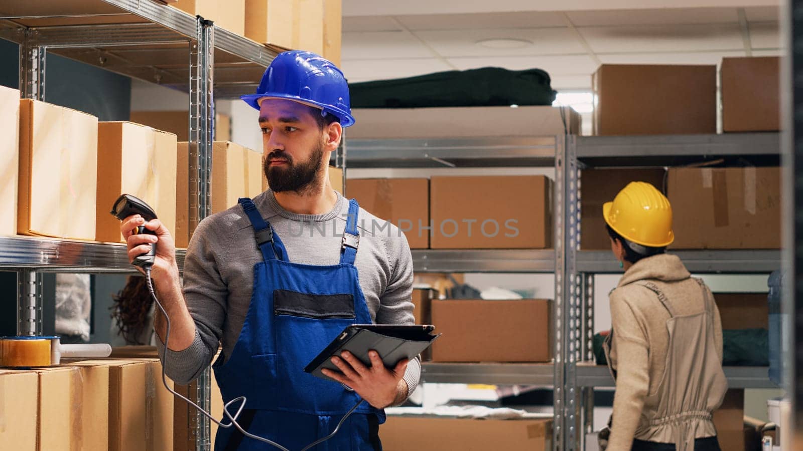 Young adult scanning barcodes on boxes in warehouse, pointing scanner at cardboard packages with goods and checking stock. Depot employee holding device in storage room, industrial job.