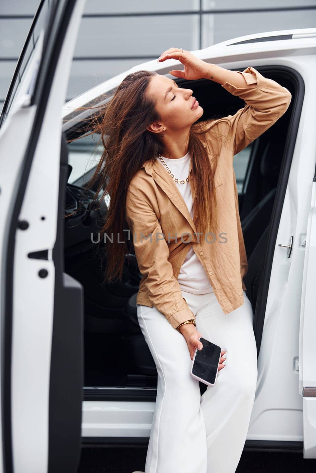 Outdoors against modern building. Fashionable beautiful young woman and her modern automobile by Standret