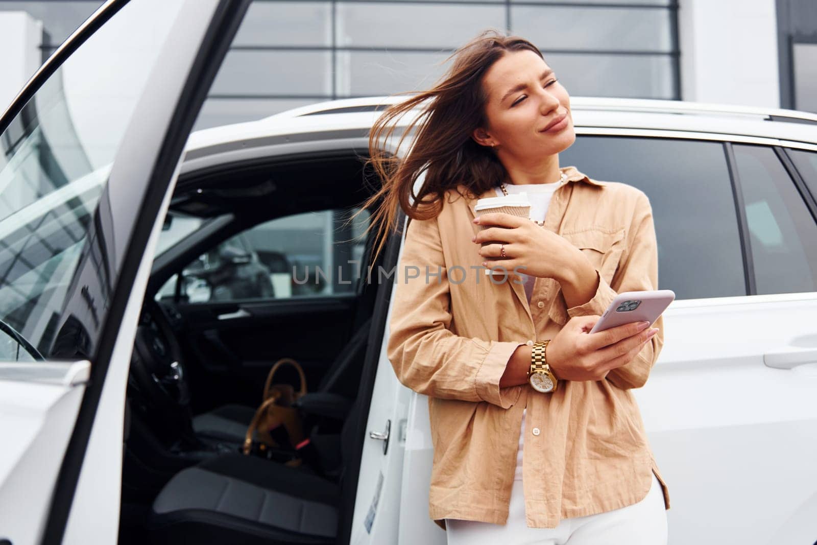 With coffee and phone. Fashionable beautiful young woman and her modern automobile.