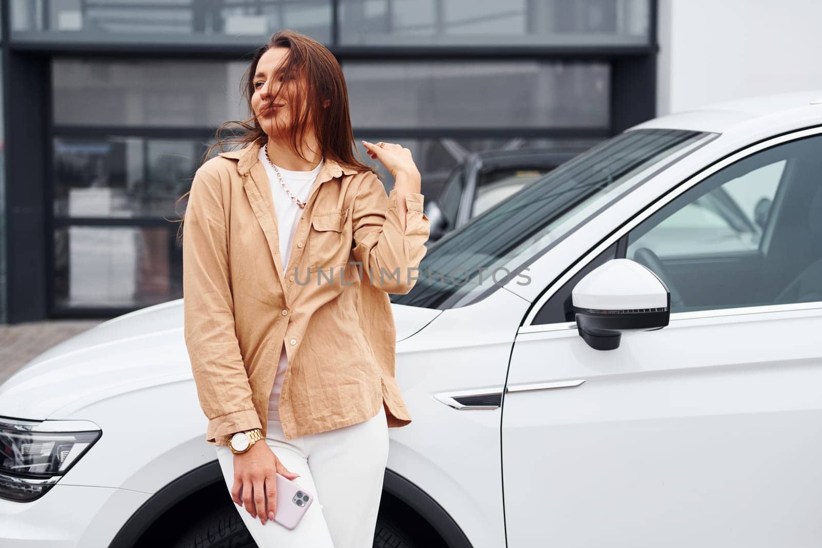 Standing outside and holds phone. Fashionable beautiful young woman and her modern automobile by Standret