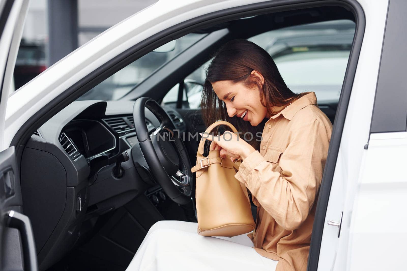 Serching something in bag. Fashionable beautiful young woman and her modern automobile.