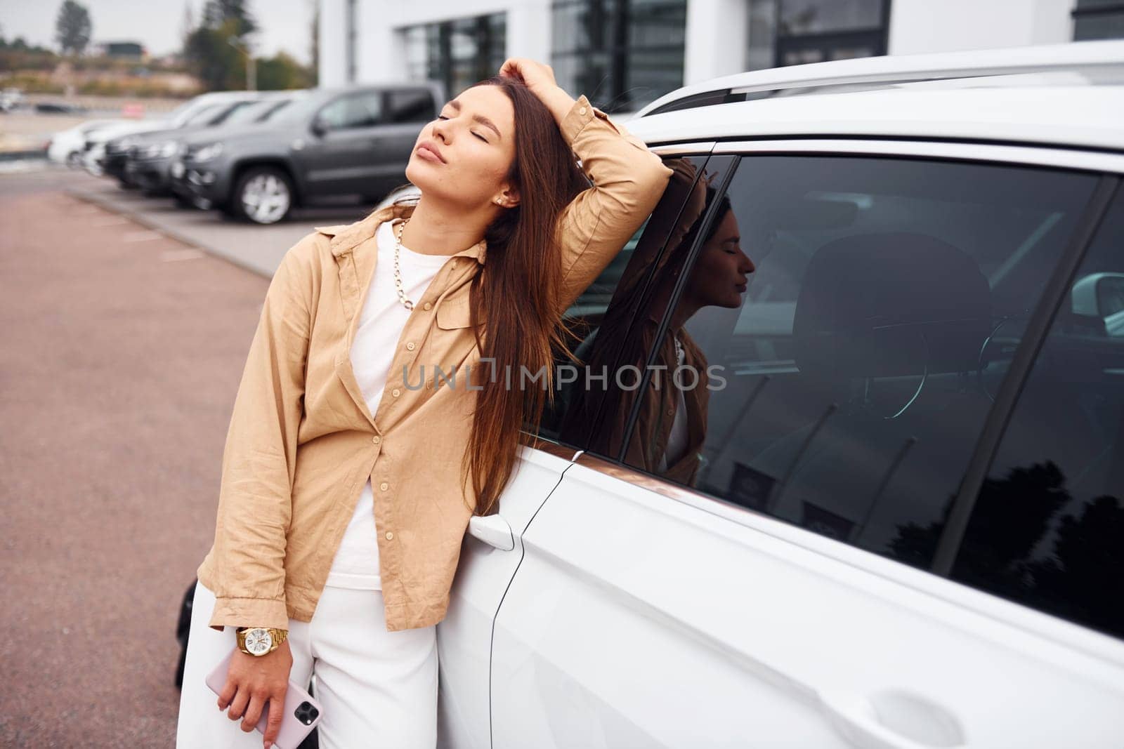 Leans on the door. Fashionable beautiful young woman and her modern automobile.