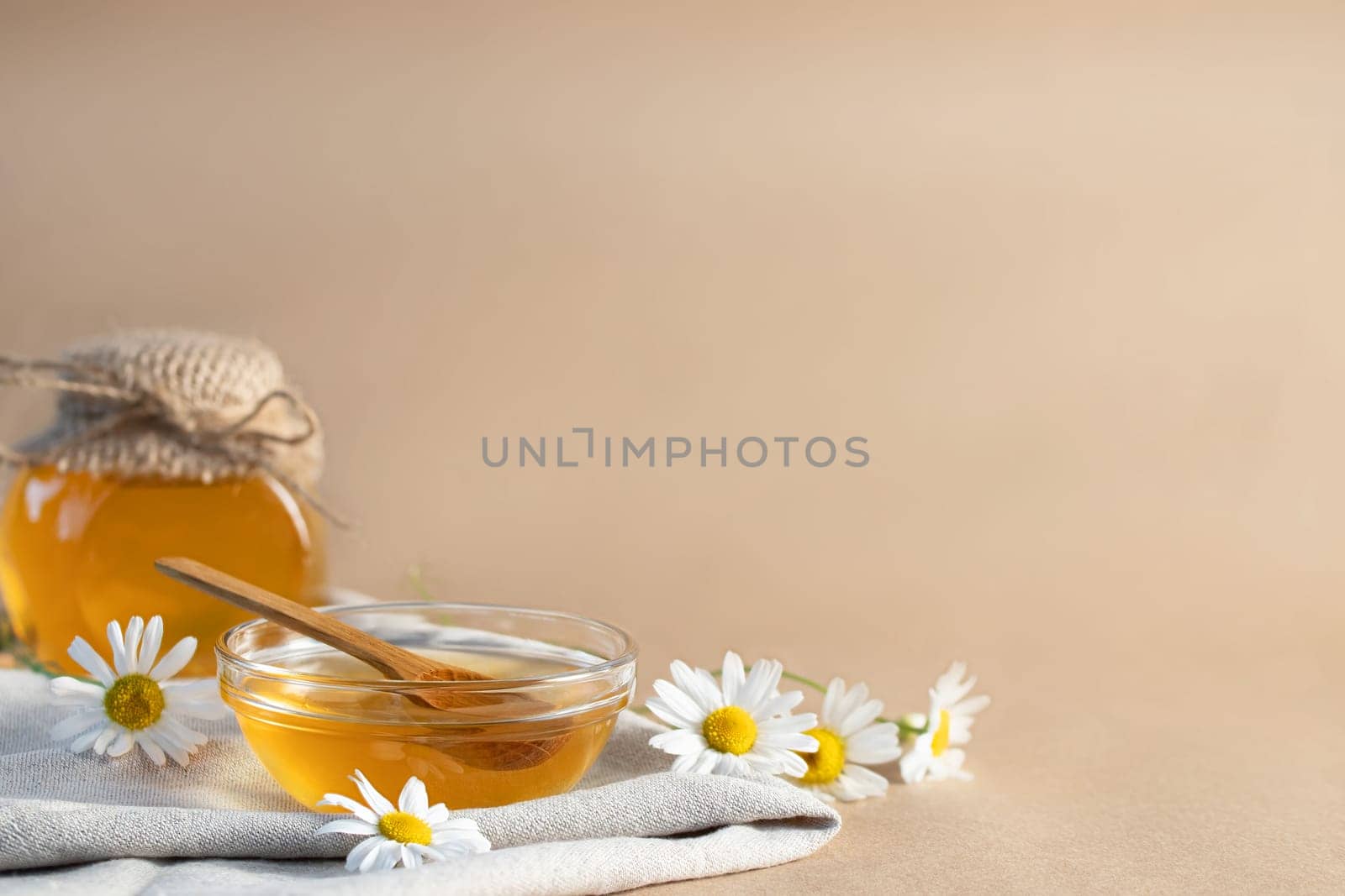 Chamomile syrup in a small bowl and in a jar and chamomile flowers on a linen kitchen towel, copy space.