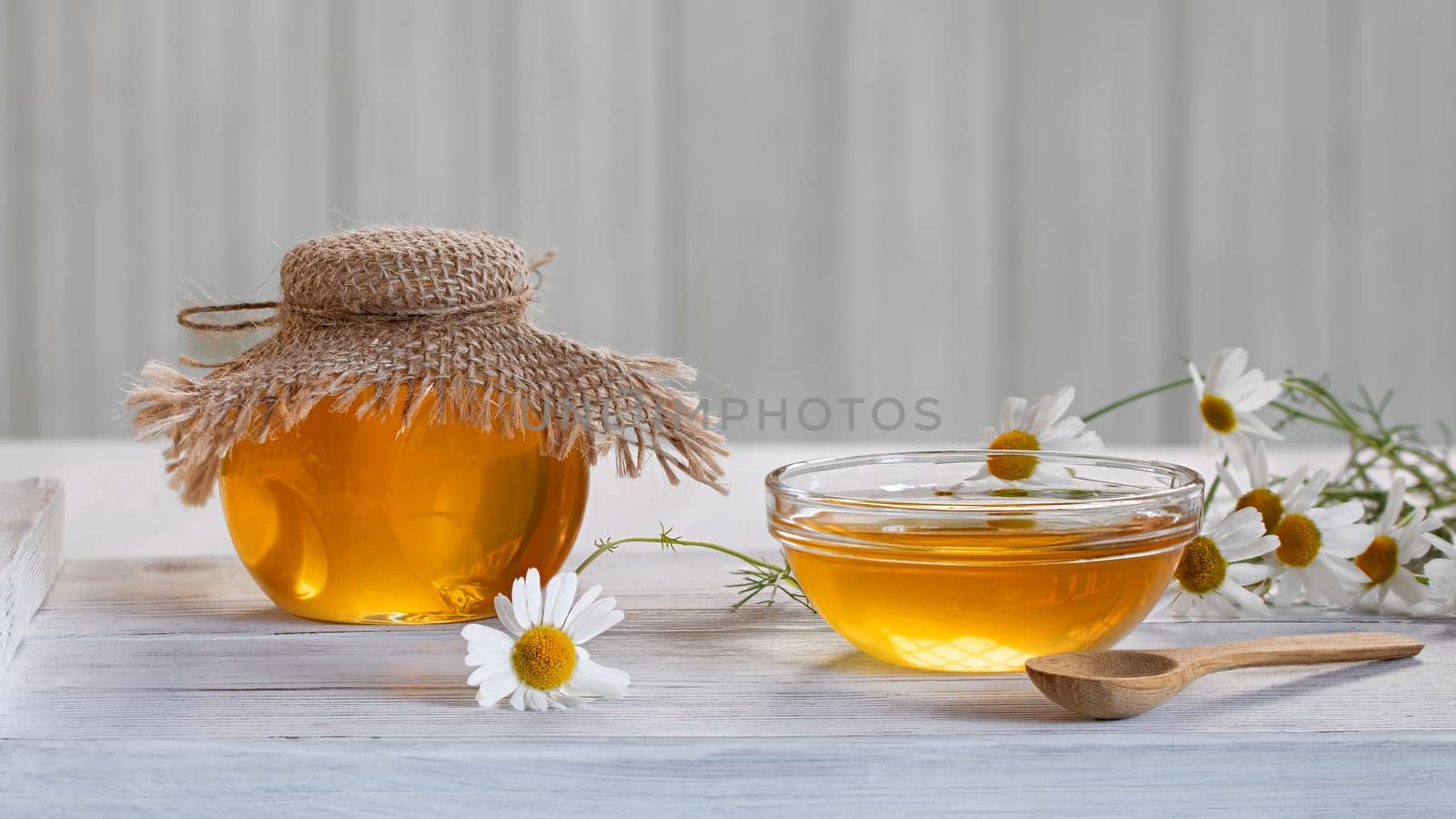Chamomile syrup in a small bowl and in a jar on a white wooden table.