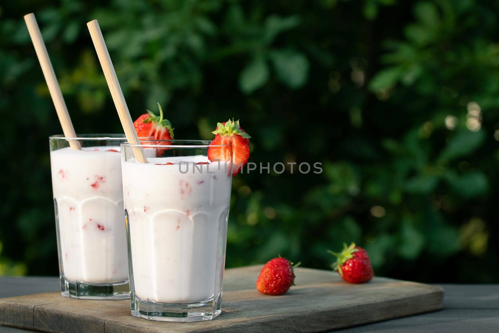 Strawberry smoothie in two glass glasses and fresh strawberries on a wooden table in the yard, copyspace by galsand