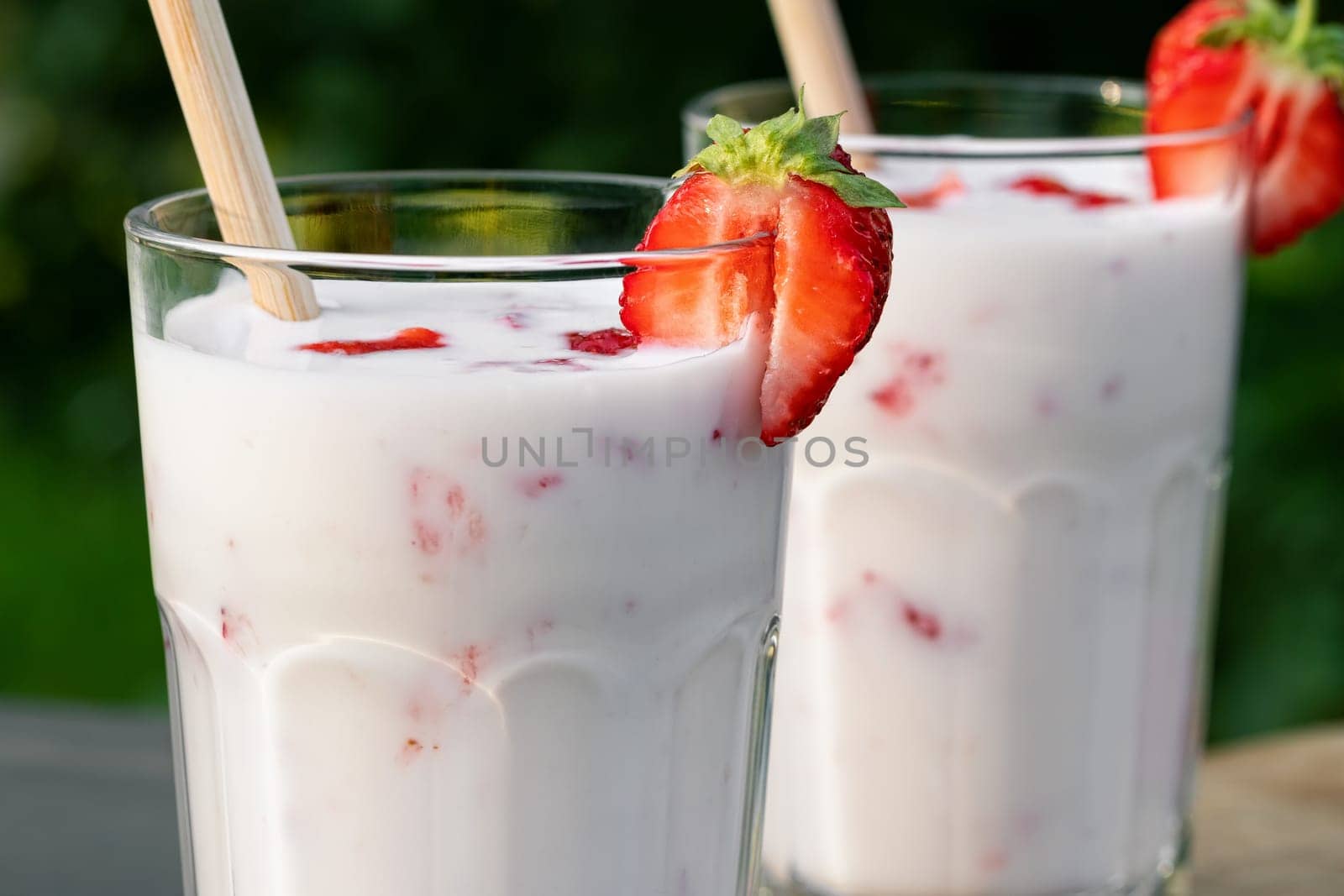 Strawberry smoothie in two glass glasses and fresh strawberries on a wooden table in the yard, close up.