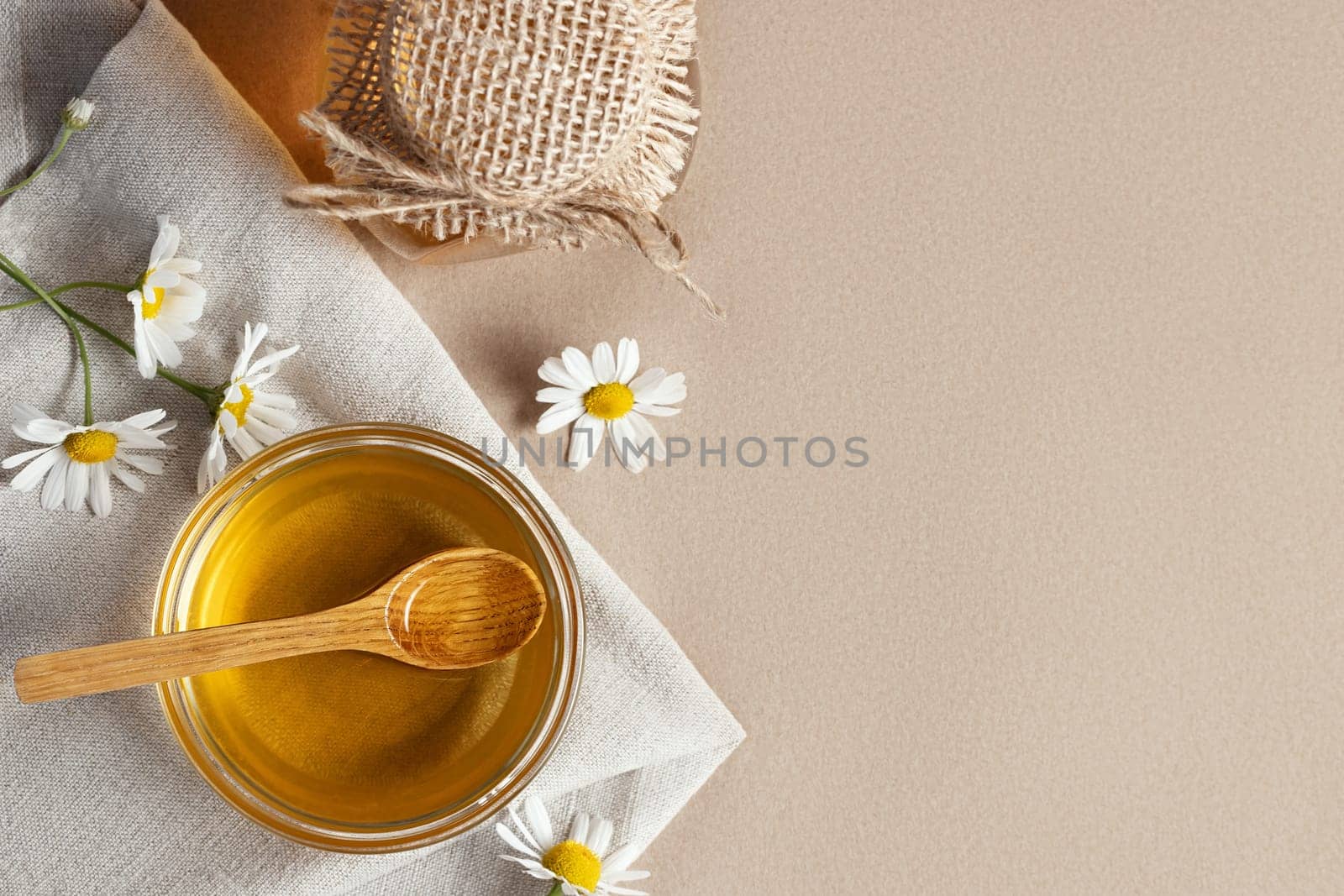 Chamomile syrup in a small bowl and in a jar and chamomile flowers on a linen kitchen towel, copy space.