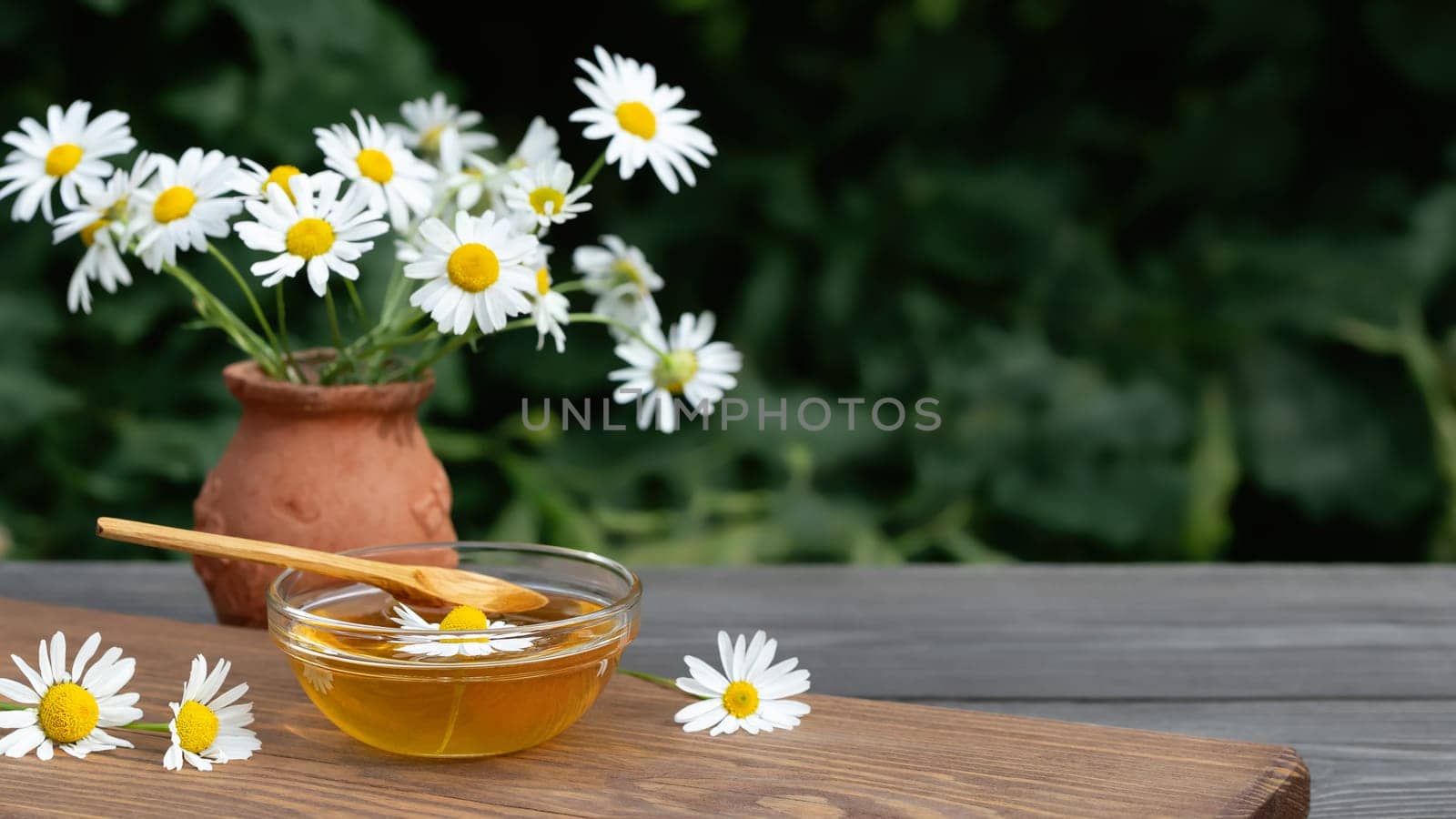 Chamomile syrup in a small bowl and in a jar in the patio on a wooden table.