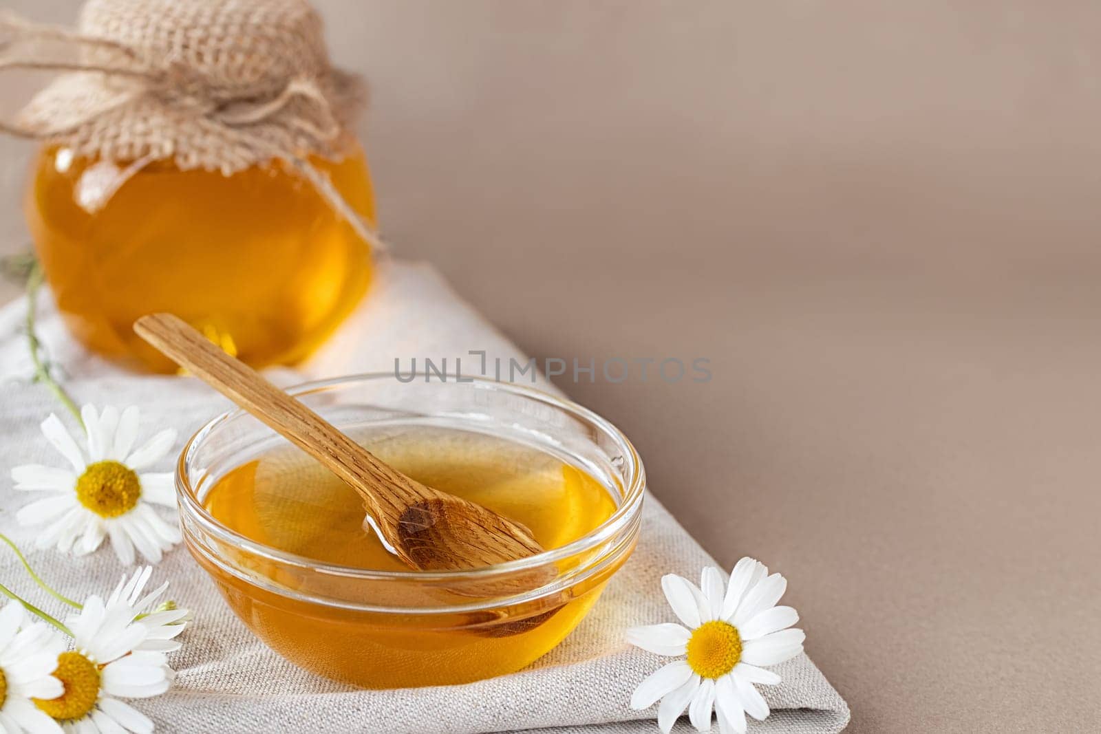 Chamomile syrup in a small bowl and in a jar and chamomile flowers on a linen kitchen towel, copy space by galsand