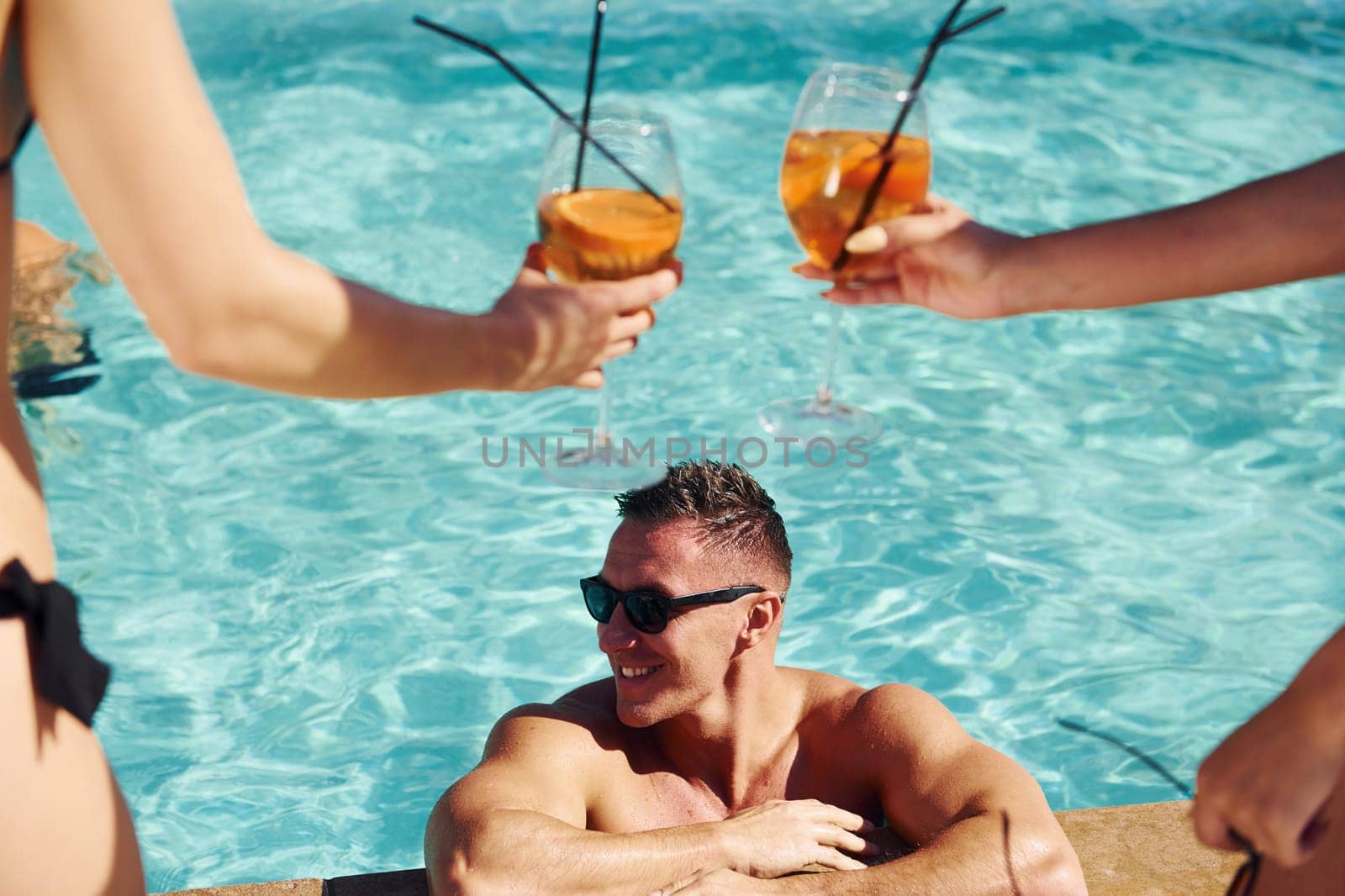 Fresh cocktails in hands. Group of young happy people have fun in swimming pool at daytime by Standret