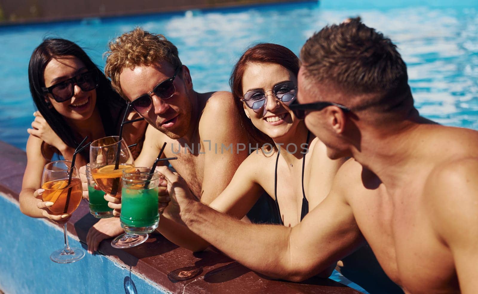 Talking and drinking. Group of young happy people have fun in swimming pool at daytime by Standret