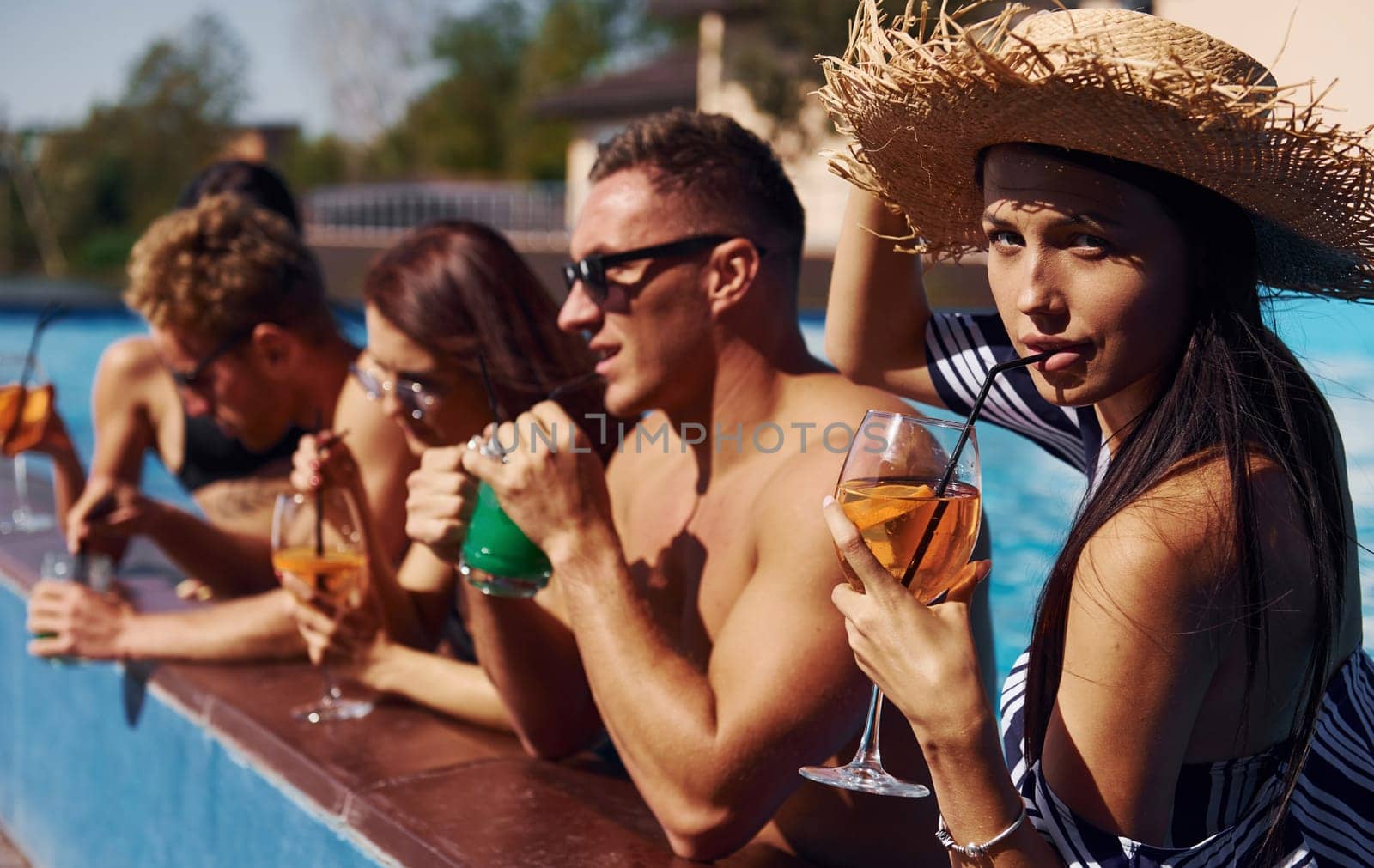 Talking and drinking. Group of young happy people have fun in swimming pool at daytime by Standret