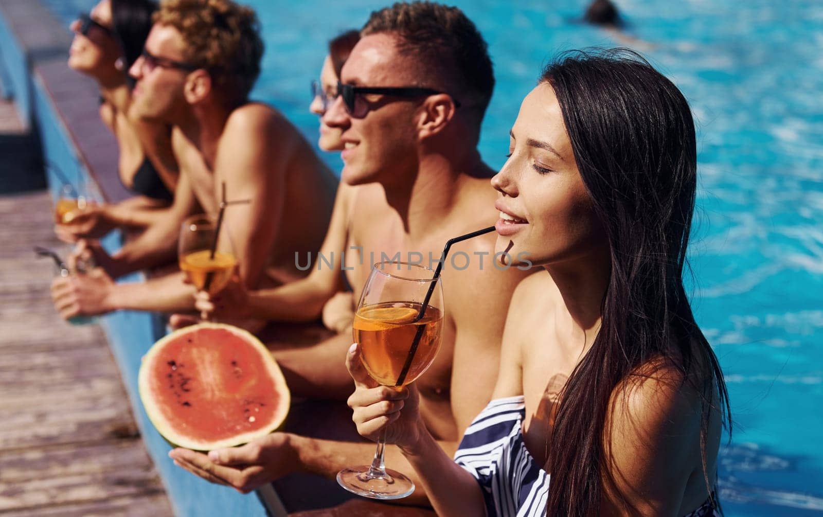 Holding watermelon. Group of young happy people have fun in swimming pool at daytime by Standret