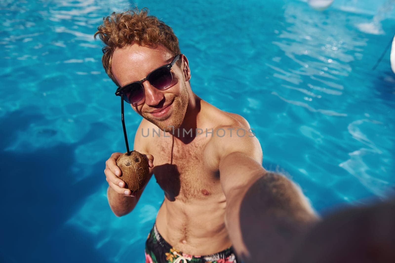 Positive young man have a rest outdoors in swimming pool at daytime by Standret