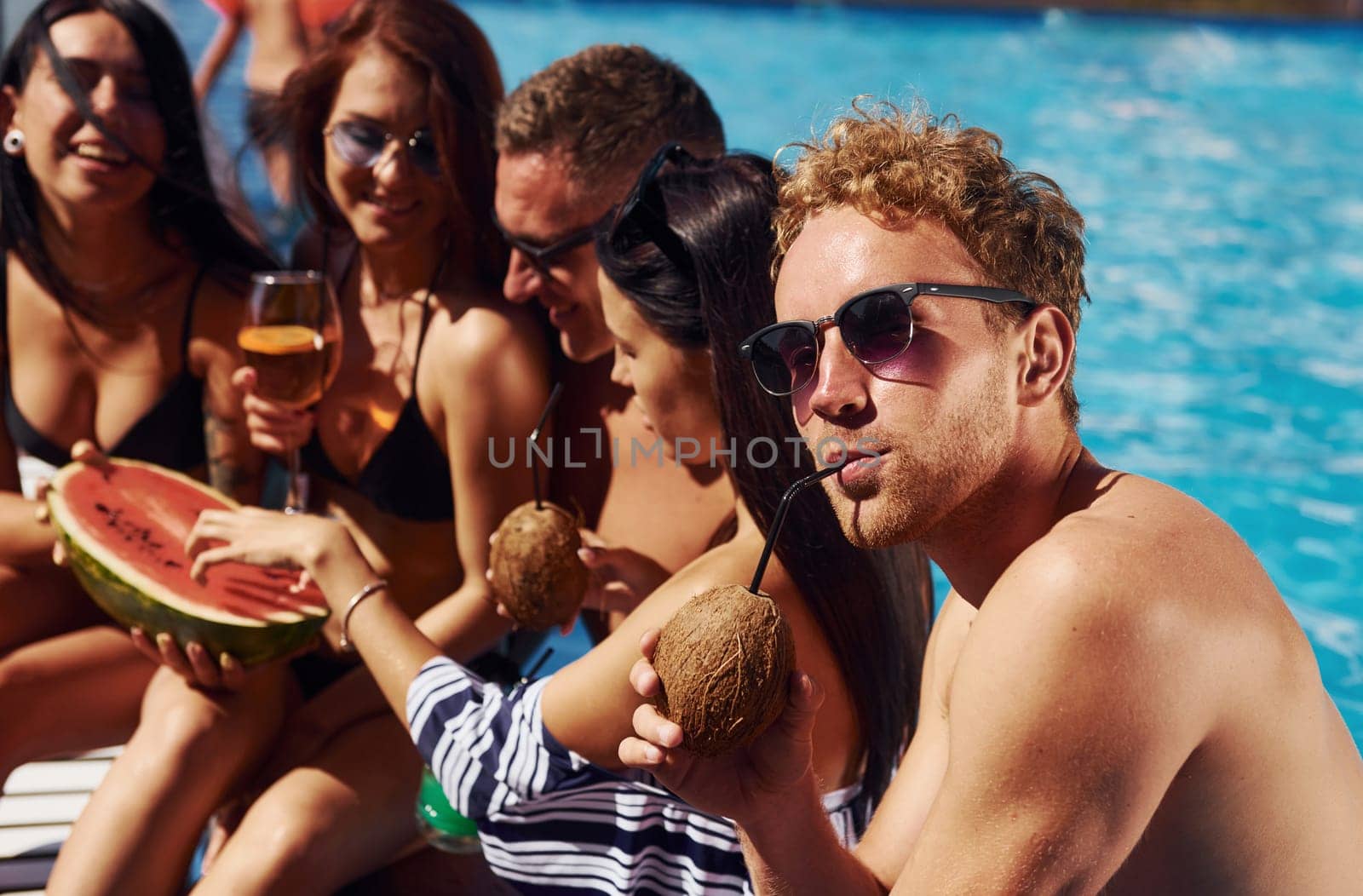 Holding watermelon. Group of young happy people have fun in swimming pool at daytime by Standret