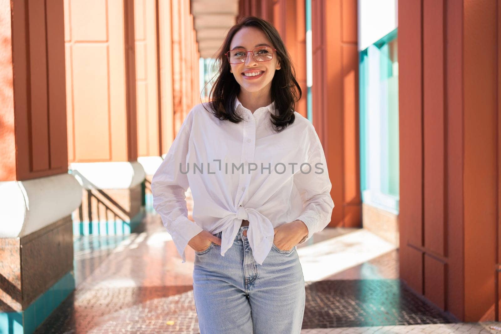Successful smiling business woman wearing eyeglasses hands in pocket. Modern businesswoman smile standing outdoor dressed white shirt and jeans. Business woman happy positive emotions