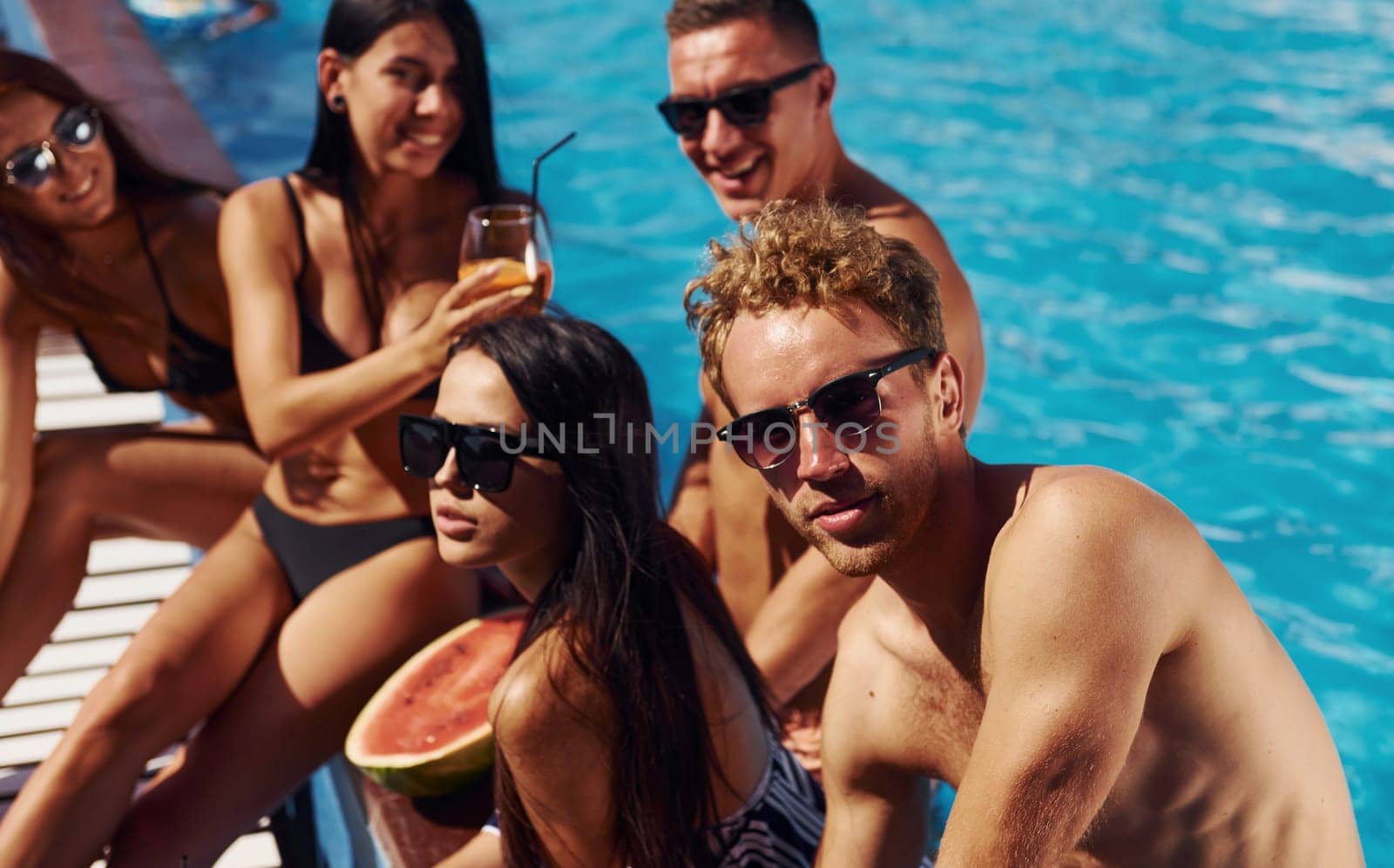 Sunny warm weather. Group of young happy people have fun in swimming pool at daytime.