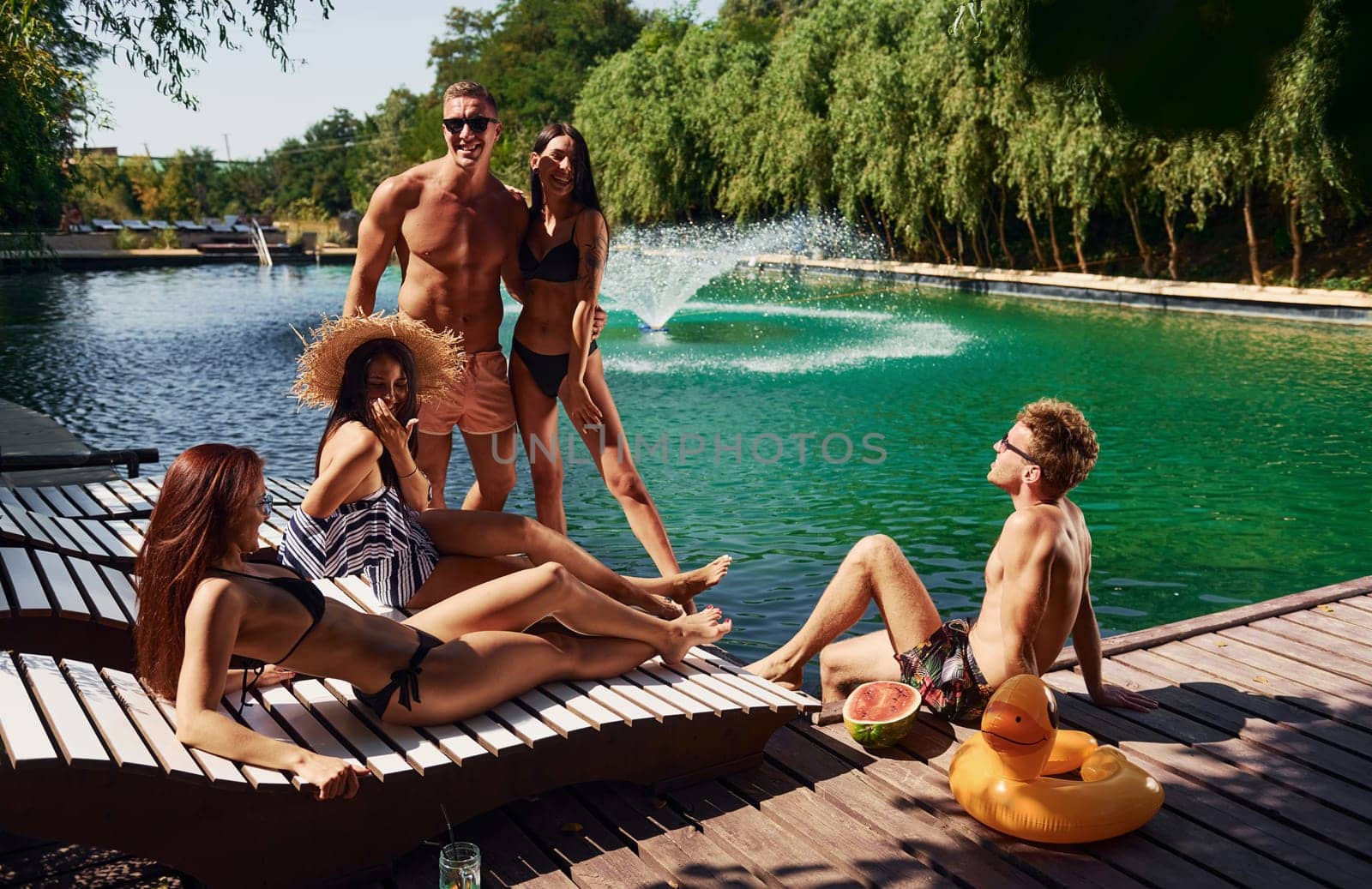 Sunny warm weather. Group of young happy people have fun in swimming pool at daytime.