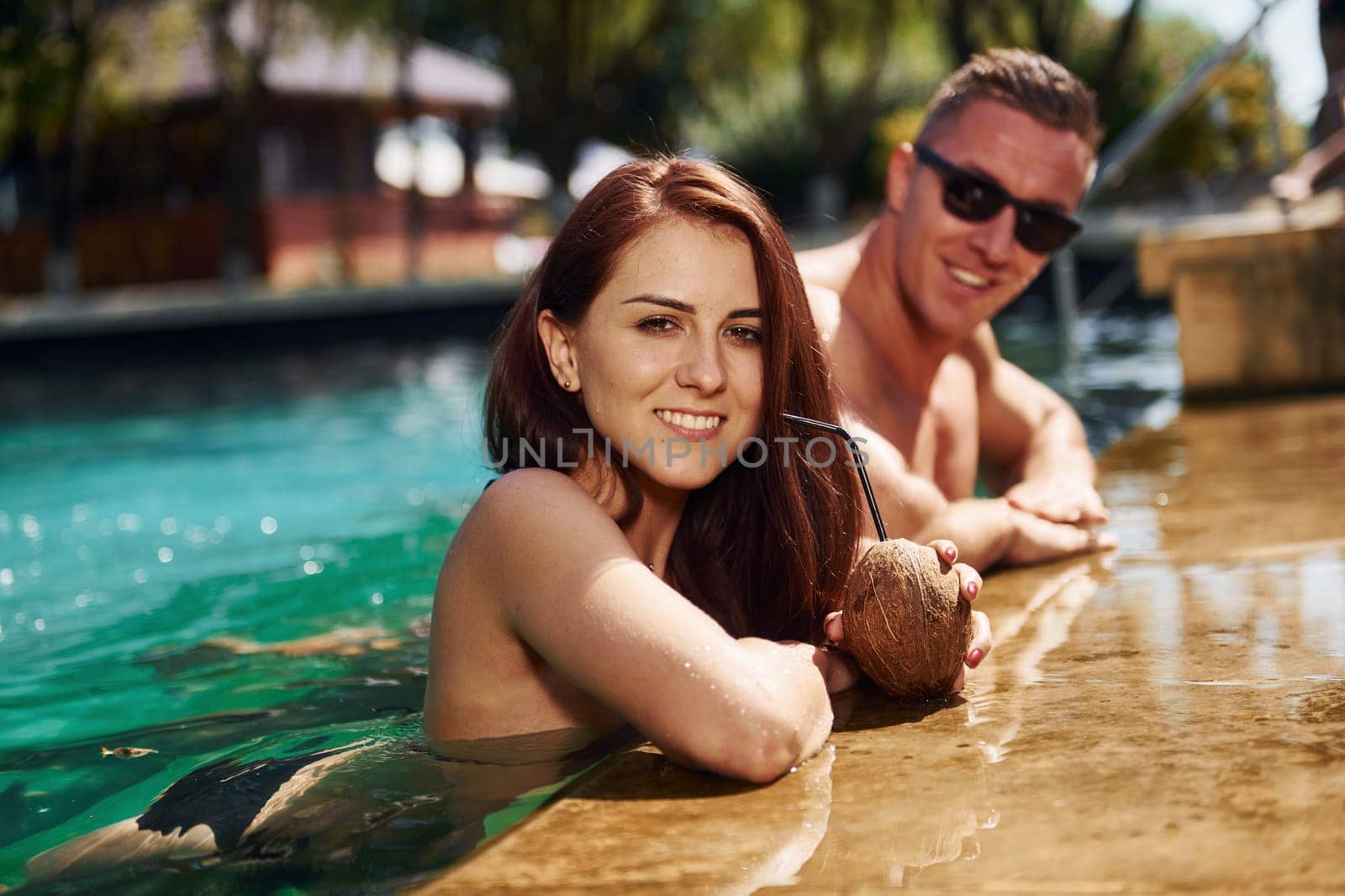 With cocktails. Cheerful couple or friends together in swimming pool at vacation by Standret