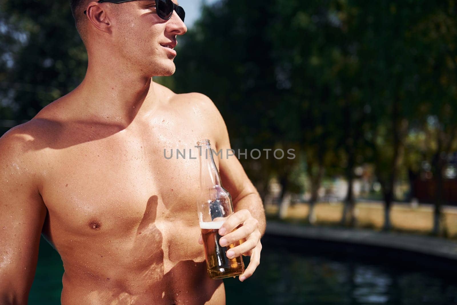 Positive young man have a rest outdoors in swimming pool at daytime.