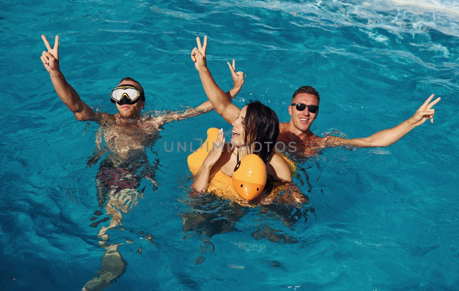 Using yellow colored duck to swim. Group of young happy people have fun in swimming pool at daytime by Standret