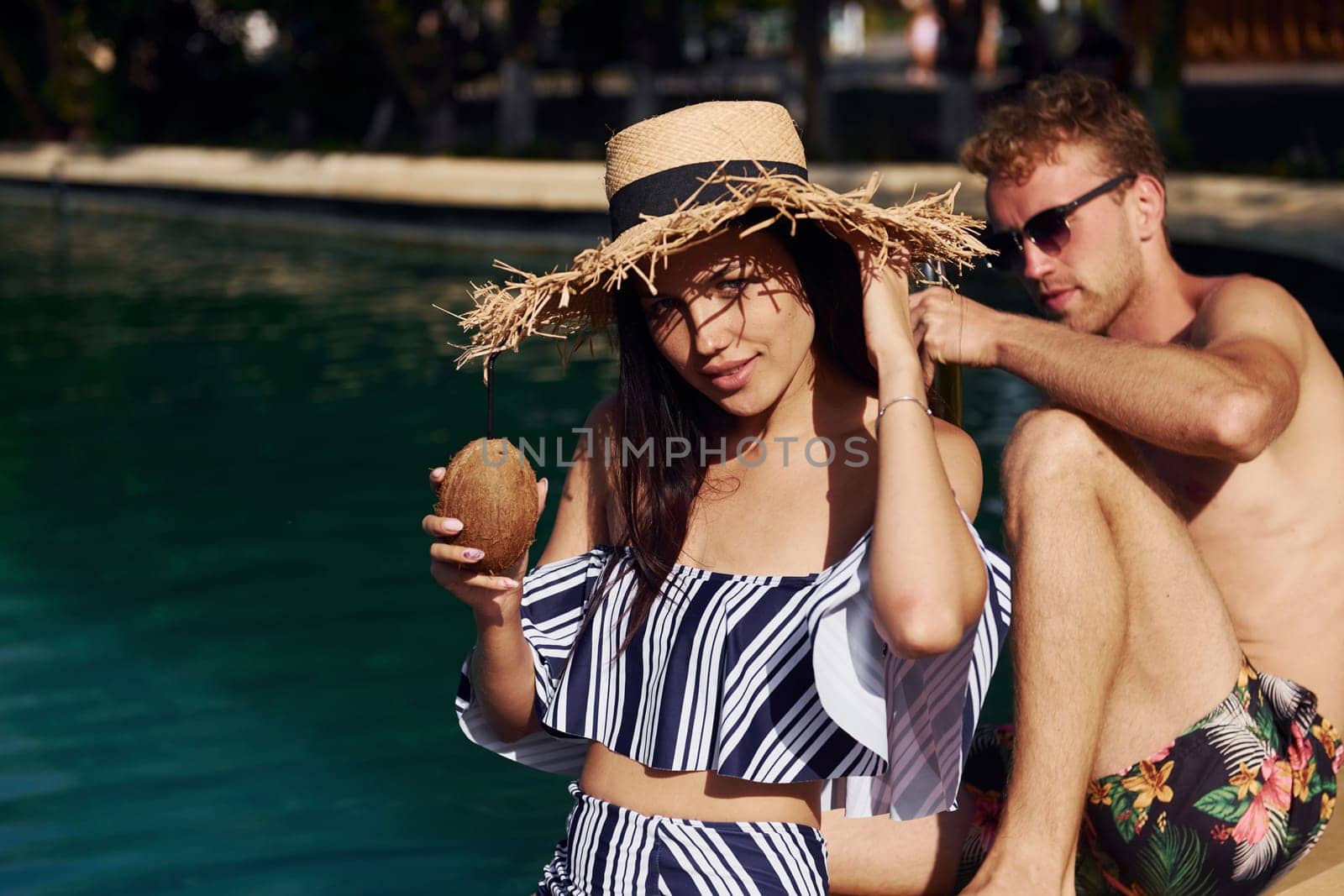 Holding drinks in hands. Cheerful couple or friends together in swimming pool at vacation by Standret