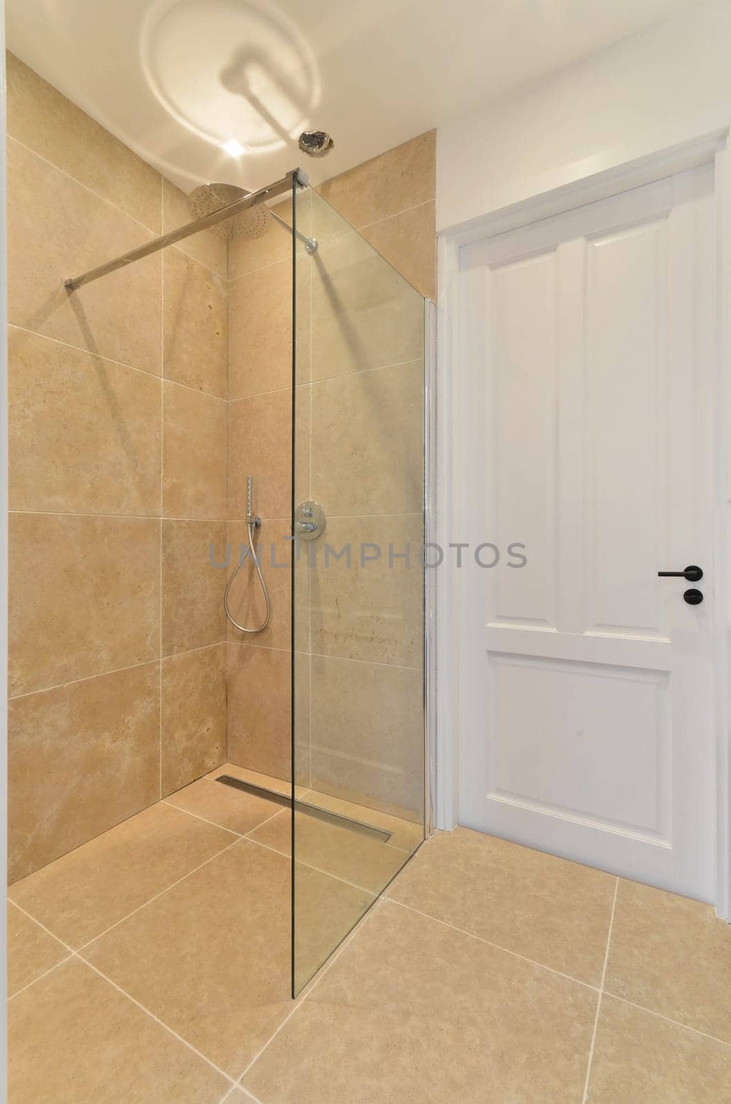 a walk in shower with beige tile flooring and white door leading to the bath room, which is tiled